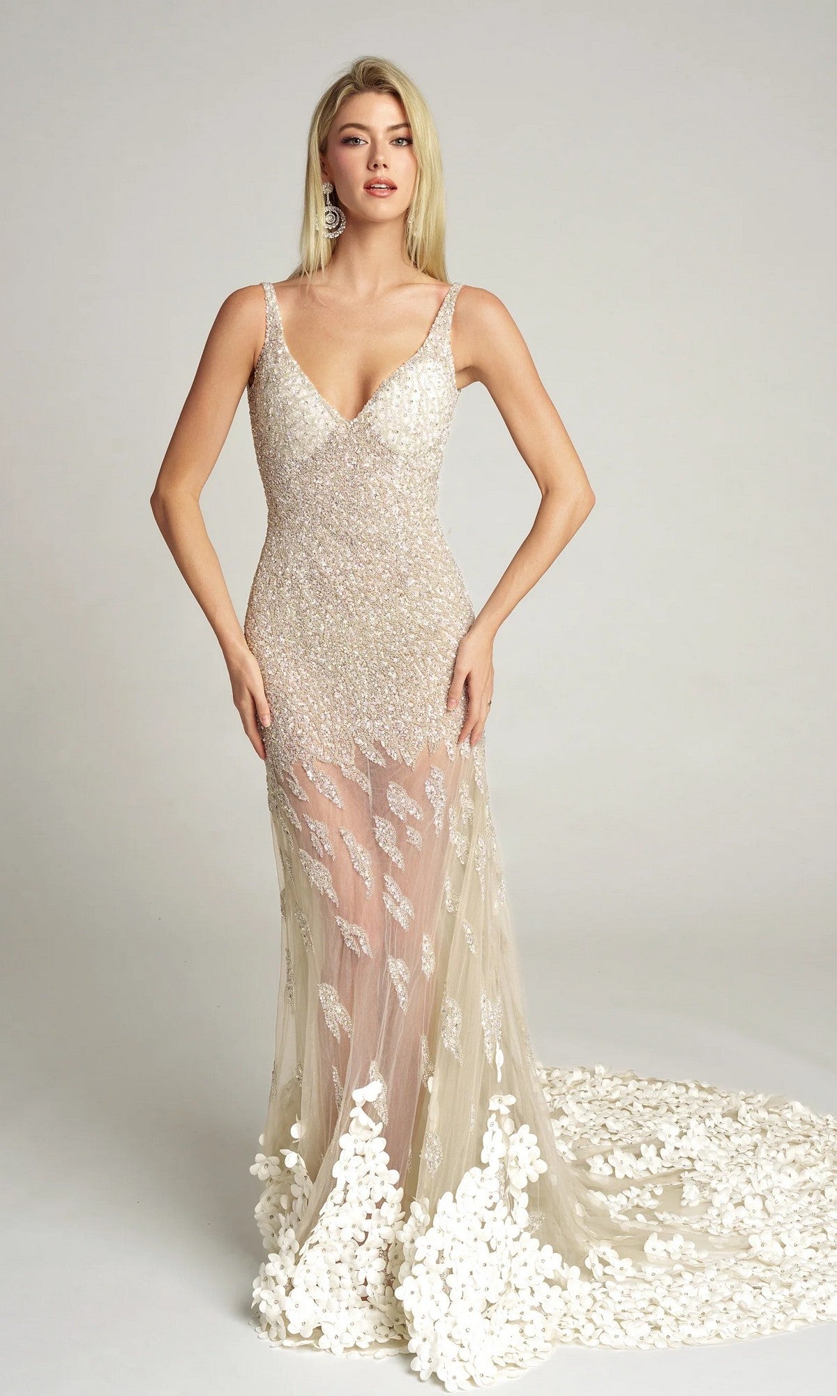 A woman stands against a plain background wearing the Portia and Scarlett PS25987C long formal dress in white, featuring a fitted bodice, illusion skirt, sequin detailing, and floral appliqué at the hem.